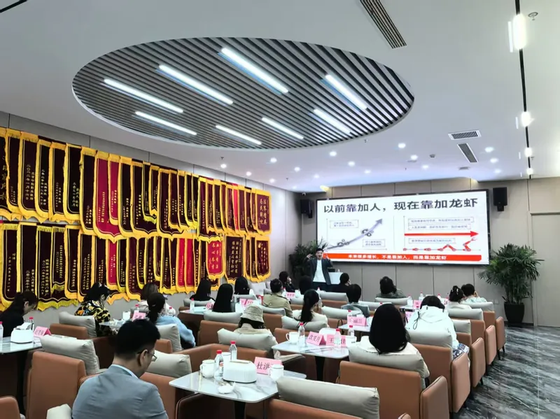 企业内训现场,左侧整面墙挂满客户送的锦旗,大屏是「以前靠加人,现在靠加龙虾」